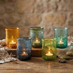 Five glass candle holders in blue, green, and amber glow on a rustic wooden table.