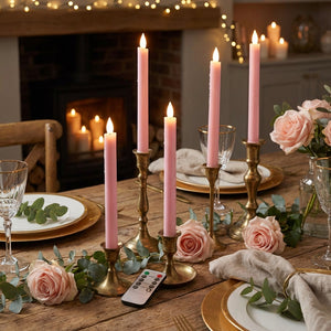 Pink candles in brass holders on a wooden table with roses, eucalyptus, and elegant tableware.