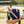 Blue bag with white and red straps, pickleball paddles, yellow balls on bench by tennis court.