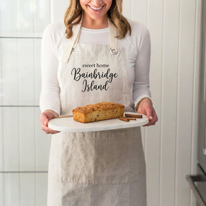 Woman in a beige apron holds a bread loaf on a white platter with cinnamon sticks.