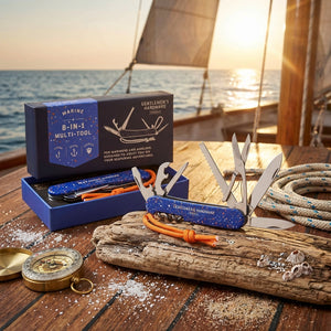 Blue multi-tool with open blades on wood, near compass and rope, with sunset over the ocean in background.