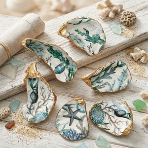 Decorative oyster shells with gold edges, painted with ocean designs on a textured white surface.
