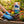 Child's hands in blue gloves planting yellow flowers in soil, surrounded by gardening tools.