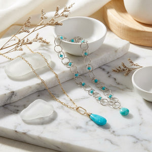 Necklaces with turquoise stones on a white marble surface, surrounded by dried plants.