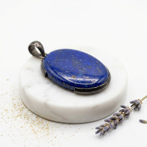 Oval blue stone pendant on white marble base with lavender sprig and gold specks.