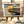 Painting of a sunset over a pier, with vibrant orange, blue skies, on an easel with art supplies.