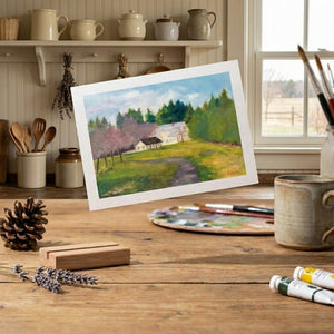Painting of a countryside scene on a table, surrounded by art supplies and rustic kitchenware.