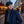 Man in blue coat and flat cap on a cobblestone street with string lights and autumn leaves.