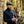 Man in a dark sweater and cap, holding a compass and notebook, leans on stone wall; bicycle nearby.