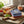 Striped towels, bread, tomatoes, lemons, and herbs on a rustic table near a steaming copper pot.