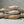 Three ceramic fish in pink, blue, and beige on driftwood with sea glass and shells around.
