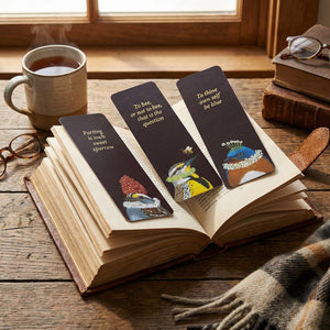 Open book with three bird-themed bookmarks, warm tones, glasses, tea cup, and cozy plaid nearby.