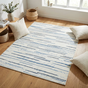 A light-colored rug with blue and gray stripes on a wooden floor, surrounded by cushions and baskets.