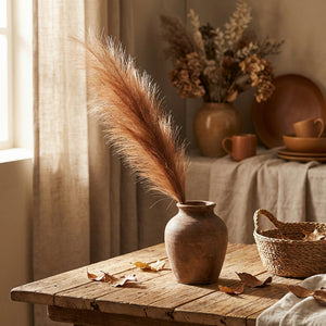 Rustic vase with pampas grass on a wooden table, warm tones, basket, and autumn leaves.