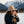 Woman in a beige hat takes a photo in snowy mountains, wearing a dark jacket and gray sweater.