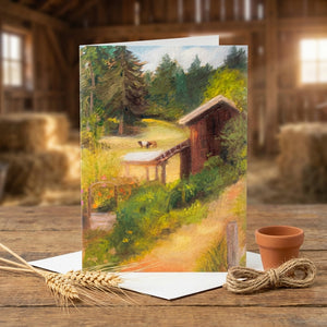 Greeting card with rustic farm scene, trees, a barn, and a goat. Warm colors, on a wooden table.