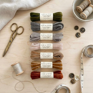 Velvet ribbons in various colors, scissors, thread spool, buttons, and measuring tape on a wooden surface.