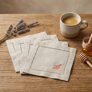 Beige napkins with pink embroidery, a mug of coffee, lavender, and honey on a wooden table.