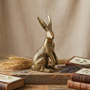 Golden hare statue on wooden block, surrounded by dried wheat, lavender, and vintage books.