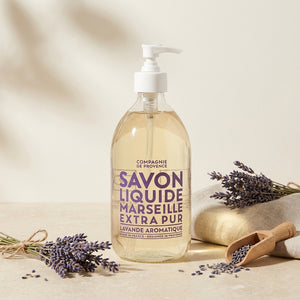 Clear bottle of lavender Marseille soap with a pump, surrounded by sprigs of lavender.