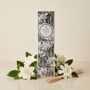 Elegant diffuser box with floral design, surrounded by white gardenias and reed sticks.