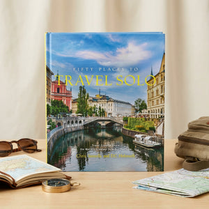 Travel book cover with a scenic river, colorful buildings, and blue sky; surrounded by travel items.