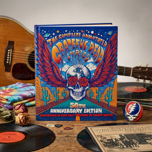Colorful book cover with a winged skull, roses, and psychedelic patterns; guitar and records nearby.