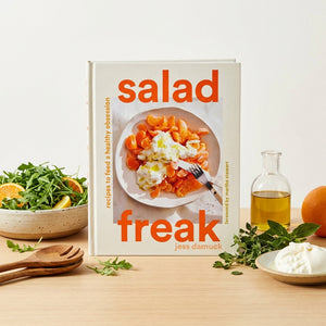 Cookbook titled "Salad Freak" with a salad, oil, greens, and wooden utensils on a table.