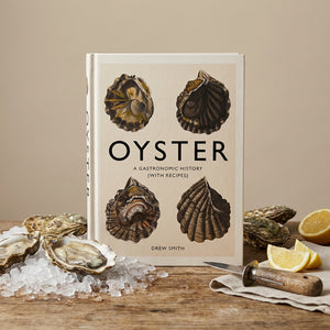 Book titled "Oyster" on a wooden table with oysters on ice, lemon wedges, and an oyster knife.