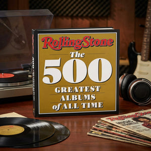 A book titled "The 500 Greatest Albums" on a table with vinyl records, headphones, and a turntable.