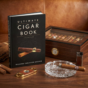 Cigar book, wooden humidor with cigars, cutter, lighter, and an ashtray on a leather surface.