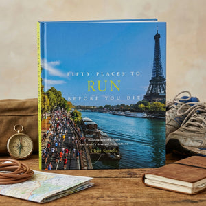 Book titled "Fifty Places to Run" with Eiffel Tower, river, and runners on cover; compass and shoes nearby.