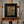 Framed landscape painting on an easel, with brushes in a jar and paint palette beside it.