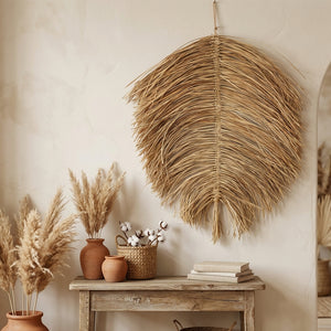 Dried palm leaf wall art above a rustic table with vases of pampas grass and cotton stems.