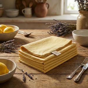 Stack of yellow linen napkins on a wooden table with lavender, lemons, and cutlery nearby.
