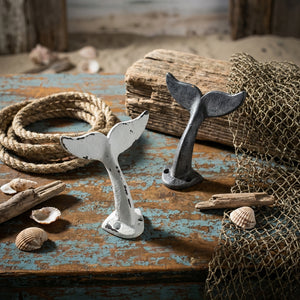 Whale tail sculptures on rustic wood table with seashells, driftwood, rope, and fishing net.