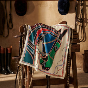 Colorful patterned scarf with ropes and horse motifs, draped on a wooden stand in a rustic room.
