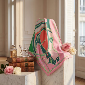 Silk scarf with green and pink patterns draped over books, beside perfume, silver horse, and roses.