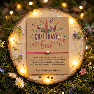 Birthday card on wood slice with unicorn, flowers, and colorful text, surrounded by fairy lights.
