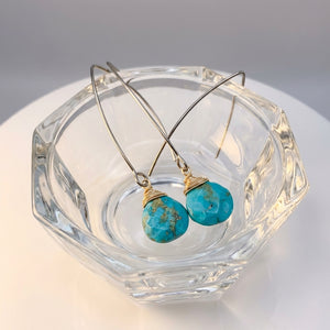 Silver earrings with turquoise stones in a clear glass bowl on a white surface.